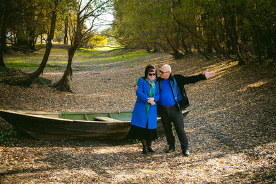 Mature couple standing on field by boat at forest