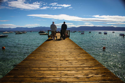 Rear view of people standing on pier over sea against sky