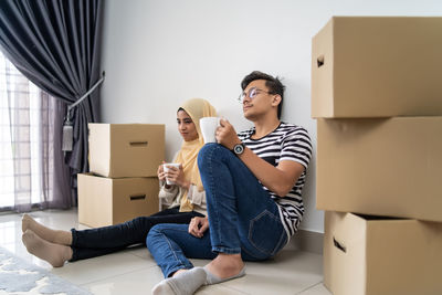 Couple having drink while sitting by cardboard boxes at new home