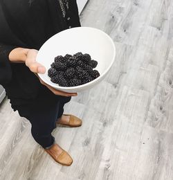 Low section of woman holding blackberries in bowl on floorboard