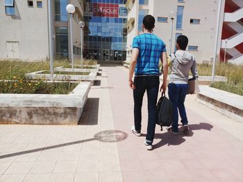 Rear view of men walking on footpath against buildings in city