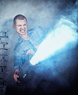 Digital composite image of angry man holding lighting equipment against brick wall