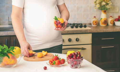 Midsection of pregnant woman with bowl of fruits