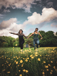 Woman with arms raised on field against cloudy sky