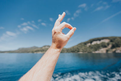 Close-up of hand against sea against blue sky