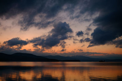 Scenic view of lake against dramatic sky during sunset