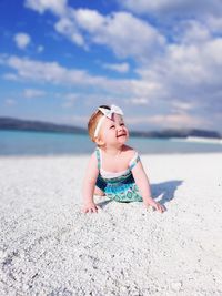 Baby girl crawling at beach against sky