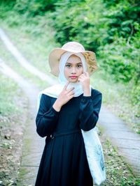 Portrait of young woman wearing hat standing against plants