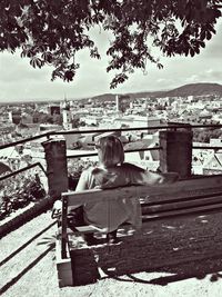 Rear view of man sitting on bench against sky