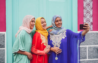 Happy female friends taking selfie by wall