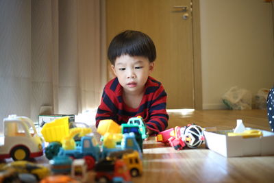 Boy playing with various toys while lying on hardwood floor at home