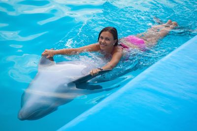 High angle portrait of smiling woman swimming with dolphin in pool