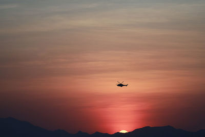 Low angle view of silhouette helicopter flying against sky during sunset