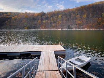 Wooden pontoon and a wooden boat on the lake surrounded by trees turning yellow in autumn