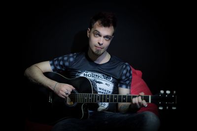 Portrait of young man playing guitar against black background