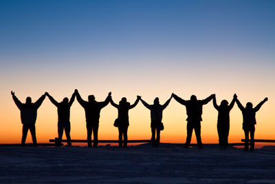 Silhouette people standing on beach against sky during sunset