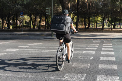 Young delivery woman with backpack riding bicycle on road during sunny day