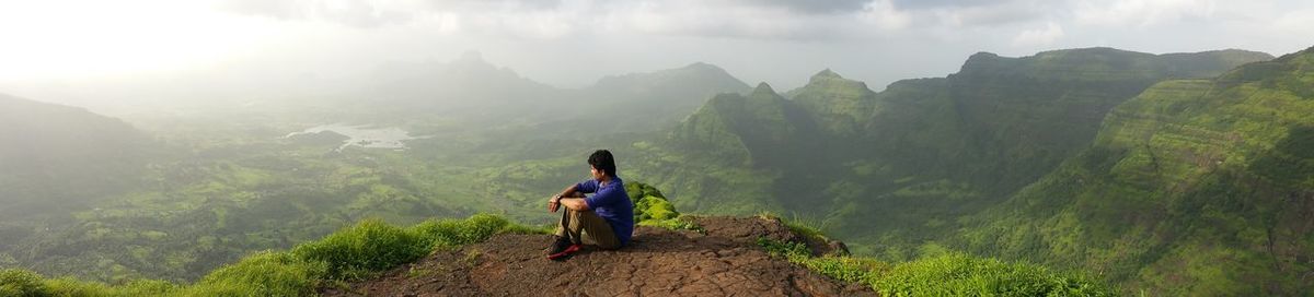 Man sitting on mountain against sky