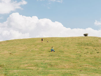 Distant anonymous children riding bicycle on grassy slope of hill while spending sunny summer day in nature against blue sky