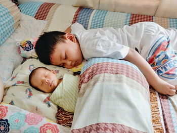 High angle view of siblings sleeping on bed at home