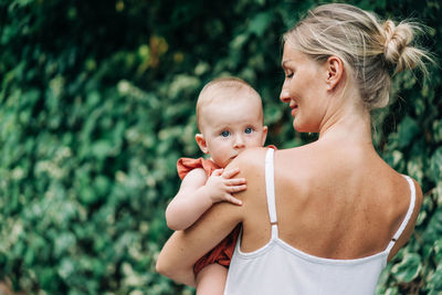 A young mother holds her baby in her arms on a walk in the summer.