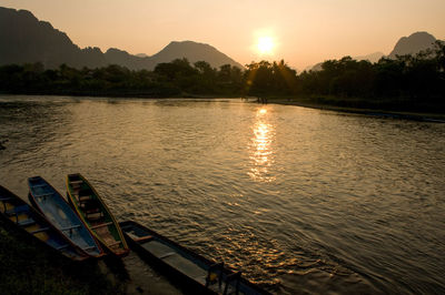 Moored boats on river with silhouette of mountain during sunset