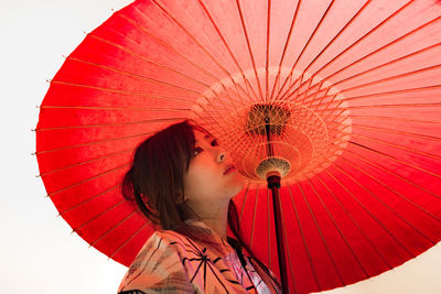 Close-up of young woman with red umbrella against sky