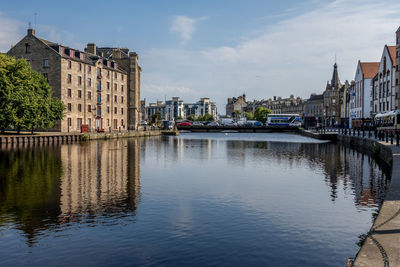 Buildings by river against sky in city