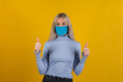 Portrait of young woman wearing mask standing against yellow background