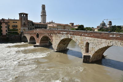 Arch bridge over river by buildings against clear sky