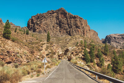 Road leading towards rocky mountains against clear blue sky