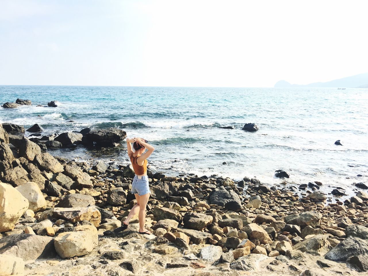 sea, horizon over water, water, beach, lifestyles, leisure activity, shore, scenics, tranquility, tranquil scene, beauty in nature, rock - object, standing, vacations, nature, young adult, sky, clear sky