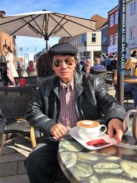 Portrait of serious man with coffee sitting at sidewalk cafe in city