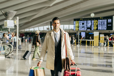 Crop of man with dark hair in stylish clothes walking with suitcase in terminal of airport