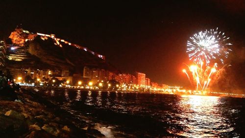 Firework display over sea against sky at night