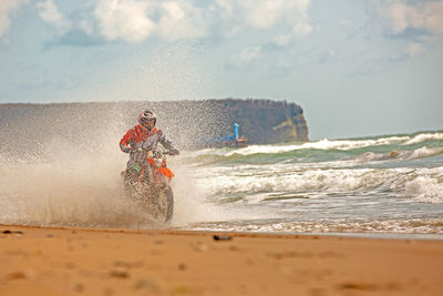 Man riding motorcycle on beach against sky