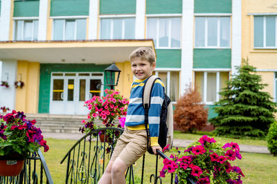 Smiling boy standing on footbridge by flower against school building