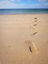 Footprints on sand at beach against sky