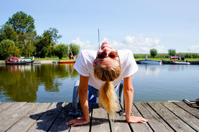 Rear view portrait of woman sitting on pier at harbor