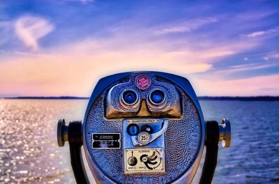 Close-up of coin-operated binoculars by sea against sky during sunset