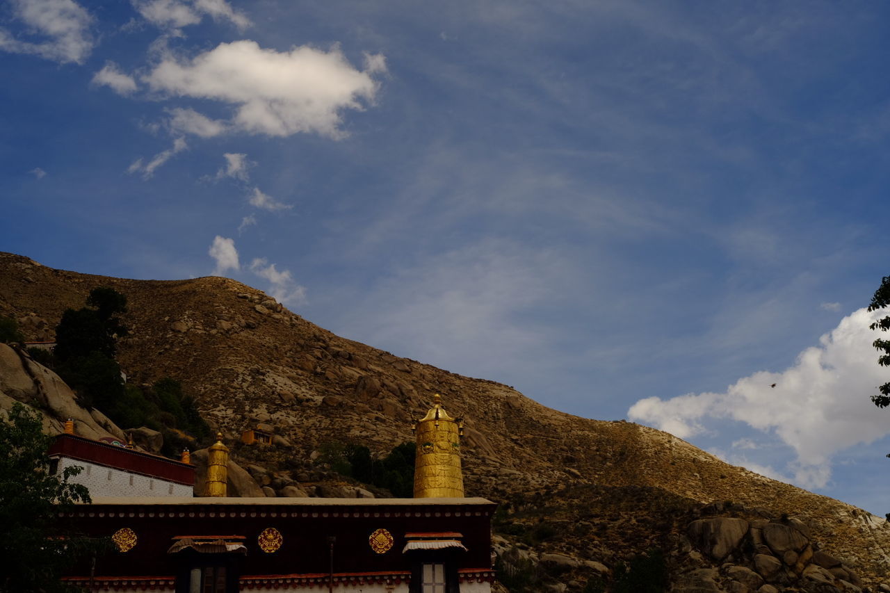 mountain, sky, cloud - sky, mountain range, low angle view, built structure, tranquility, architecture, scenics, tranquil scene, nature, tree, cloud, beauty in nature, rock - object, history, rock formation, day, outdoors, cloudy