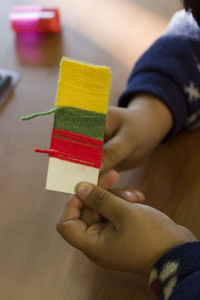 Cropped hands of boy rolling woolen strings on strip