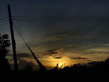 Low angle view of silhouette electricity pylon against dramatic sky