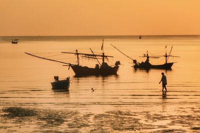 Man walking in sea against sky during sunset