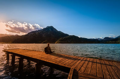 Man sitting on pier over sea against sky