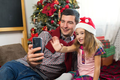 Happy young woman using mobile phone while standing on christmas tree