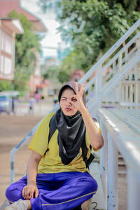 Portrait of smiling young woman wearing hijab sitting on bench in city