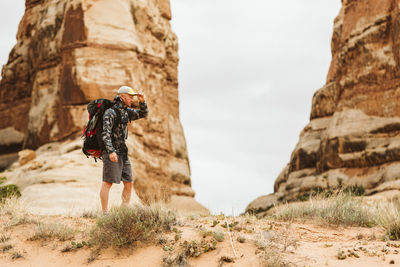 Hiker with big backpack pauses under red rock structures in utah