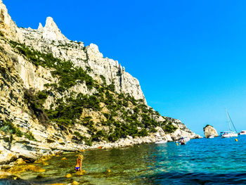 People on rock by sea against clear blue sky