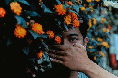 Portrait of young man covering face with hand while standing by plants